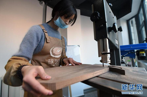 宋乐乐在木艺工作室里使用电锯帮助体验者加工木艺模型(1月10日摄)